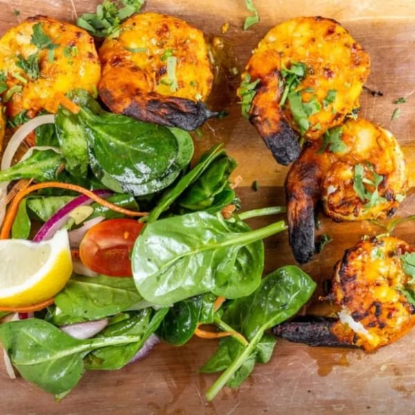 Flambé India's grilled Indian prawns with charred tails, fresh spinach salad, and a lemon wedge.