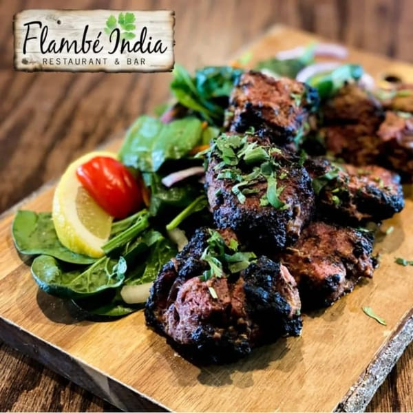 Grilled Indian meat dish with fresh greens, lemon, and tomato on a wooden board.