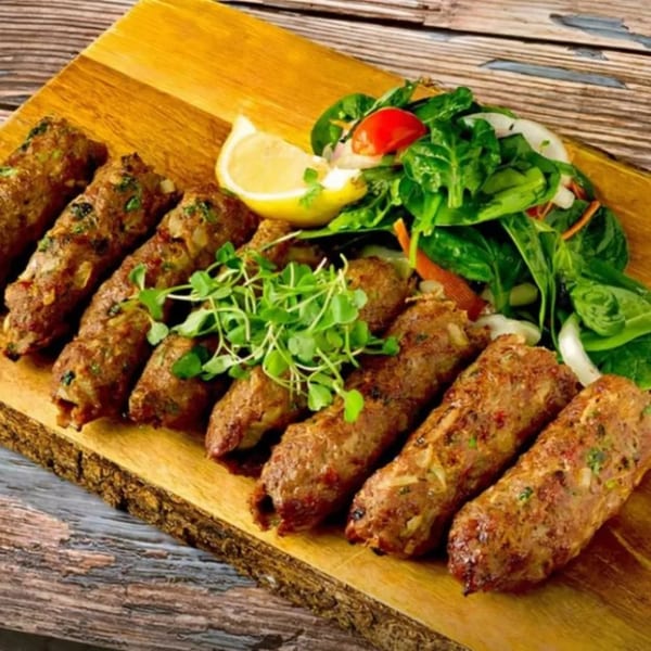 Flambé India's seekh kebabs, garnished with microgreens, lemon, and a fresh side salad on a wooden board.