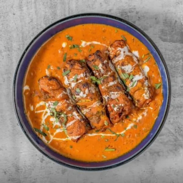 Four pieces of Indian chicken tikka in a rich orange sauce, drizzled with cream and garnished with herbs.