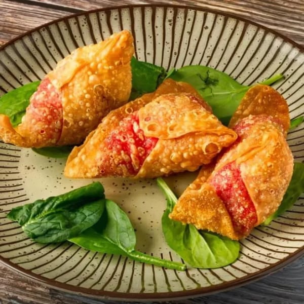 Three crispy fried Flambé India samosas with vibrant red filling, garnished with fresh spinach on a striped plate.