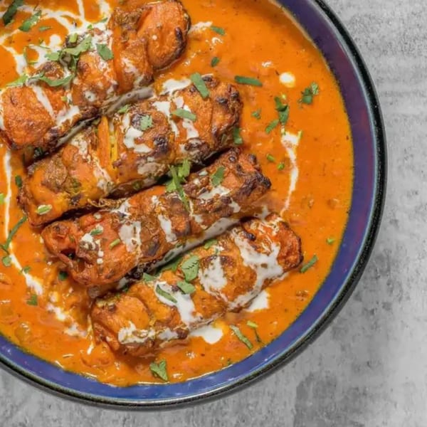 Flambé India's chicken tikka masala, garnished with cream and cilantro, in a blue bowl.