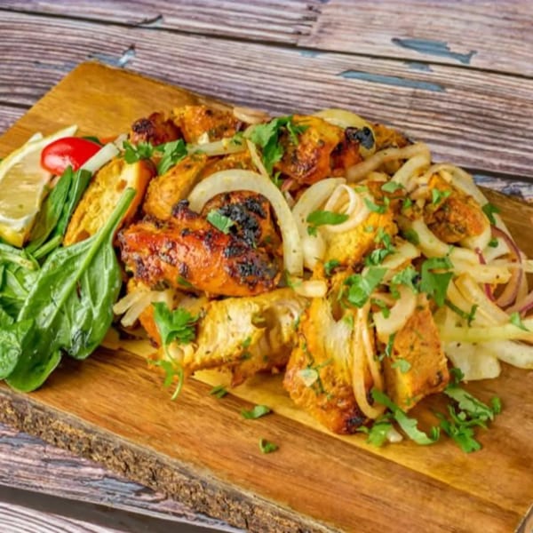Indian chicken tikka with onions, cilantro, lemon, and spinach on a wooden board.