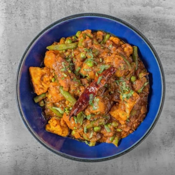 A vibrant Indian curry with paneer, green beans, and peas, garnished with cilantro and a red chili.