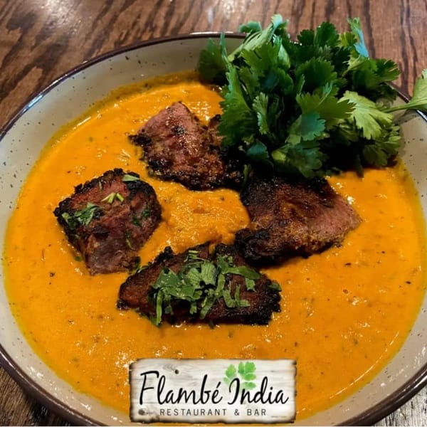 Flambé India's Indian dish with seared meat in a rich orange sauce, garnished with fresh cilantro.