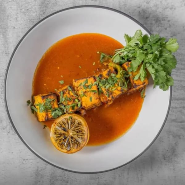 Indian paneer tikka in a rich orange sauce, garnished with fresh cilantro and a grilled lemon.